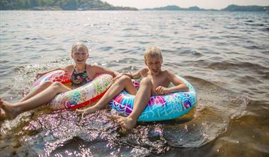 To barn som koser seg i vannet på hver sin badering