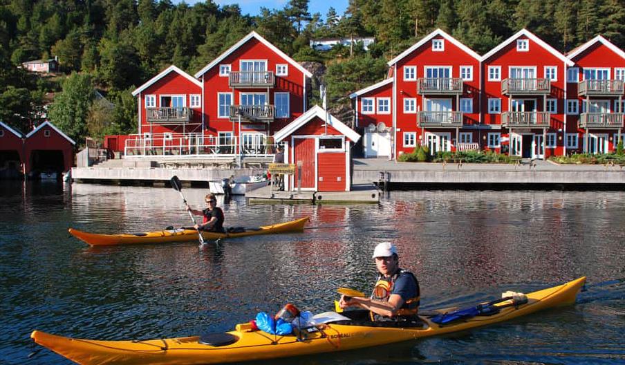 Bilde fra vannet mot de røde bygningene på Tregde, med to personer i hver sin gul kajakk