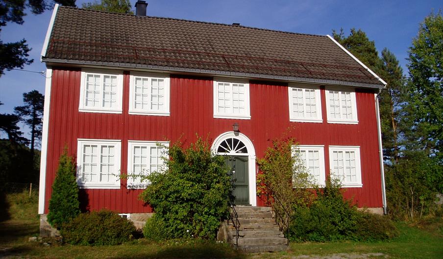 Annen rød bygning med hvite karmer, 9 vinduer og 1 grønn dør