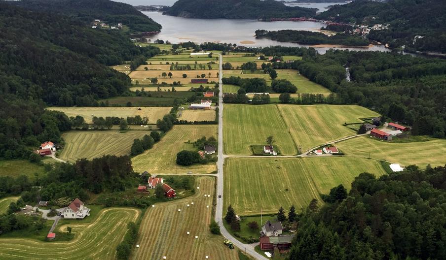 Bilde tatt ovenfor av en vei midt på med åkere og hus på høyre og venstre side