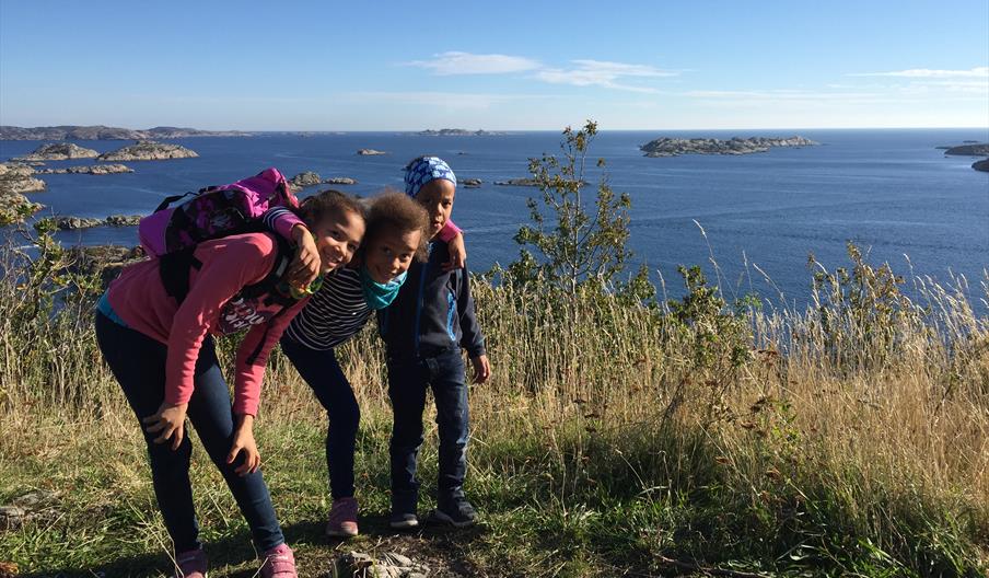 Tre barn på toppen av utsiktpunktet med havet bak seg og åpen himmel
