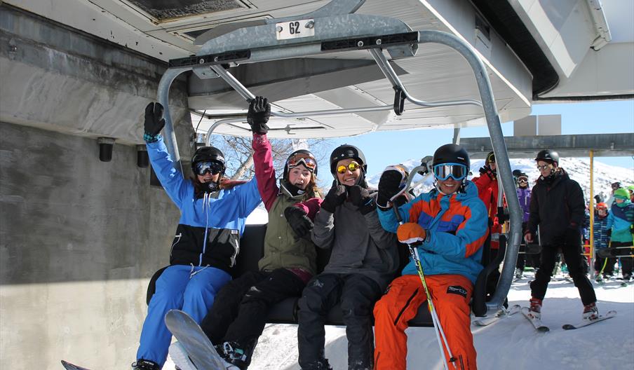 Fire glade ungdommer med ski sitter i stolheisen, bilde