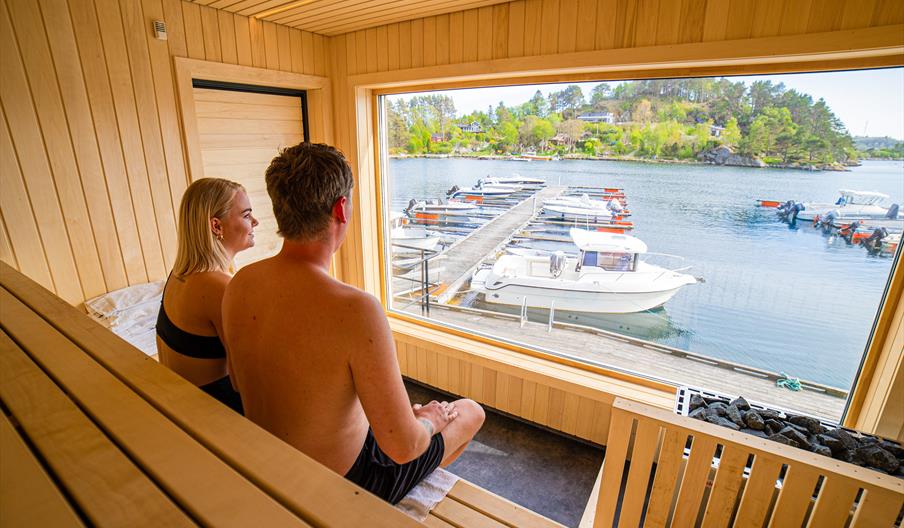 sauna-badstue-tregde-mandal-bading-skjærgård-utsikt. To personer i badstue hos Tregde Sauna. Foto.