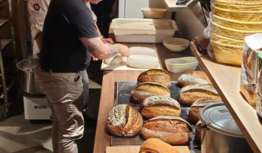 To smilende menn, som baker brød. Flere nystekte brød på benken foran dem.