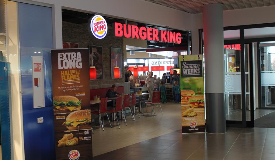 inngangen til Burger king, Alti Mandal. Store bokstaver ved taket "burger king" + logo. høye bannere på hver sin side av inngangen med bilde av burgere.