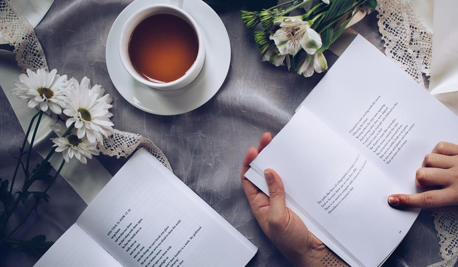 Bord med kaffekopp og person som leser bok.