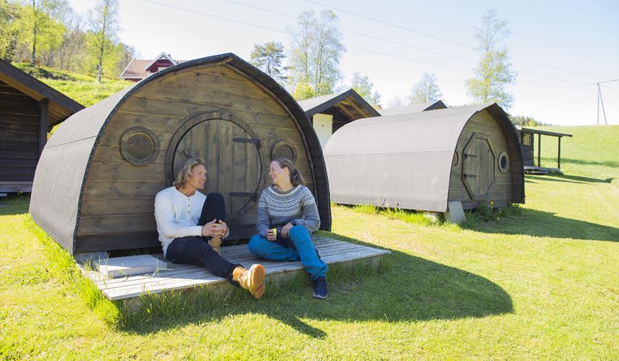 Jente og gutt sitter å ler sammen foran en av hobbithyttene til Adventure Norway