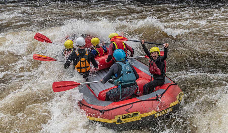 Rafting i Mandalselva, en glad gjeng i bølgene. Et barn som roper av glede og løfter åren over hodet