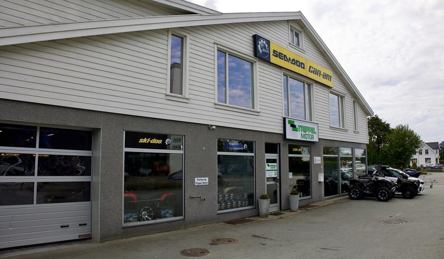 Fasaden til Trippel Motor Lyngdal i Alleen, med logo og utstilte ATV-er foran butikken.