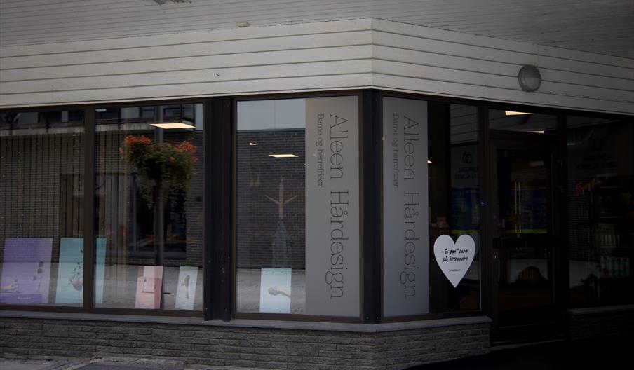 Fasaden til Alleen Hårdesign i Lyngdal sentrum, med store vinduer og tydelig skilt ut mot gata.