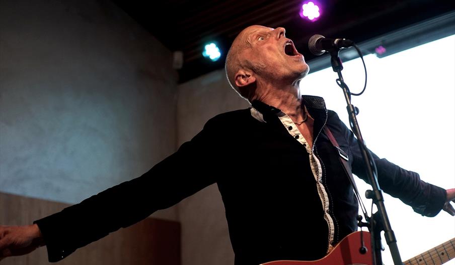 Chris Erichsen bak mikrofonstativ med gitar, åpen munn og armene ut til sidene@ Munken Bar og Scene