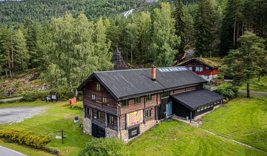 flyfoto av Hillestad galleri, en tømmerbygning omgitt av grønt gress og skog.