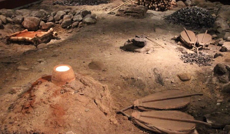 Bilder av rekonstruert jervinnetuft med smelteovn og blåsebelger, røstet jernmalm og kolgrop med trekull.