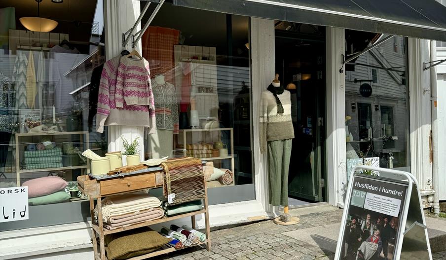Fasade til butikken Husfliden i gågata, med åpen dør og flotte utstillinger av strikkede gensere