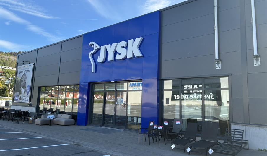 Fasaden til JYSK Lyngdal i Handelsparken, med blå logo og utemøbler utstilt foran inngangen.