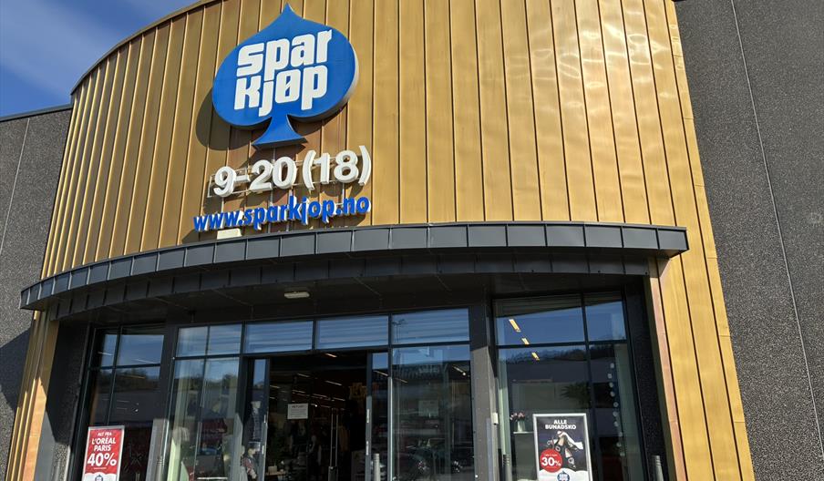 Inngangen til Sparkjøp Lyngdal i Handelsparken, med gullfasade og logo over døren.