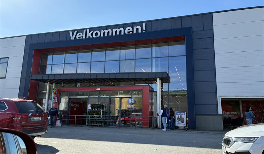Inngangen til Coop Obs Hypermarked Lyngdal i Handelsparken, med rød inngangsparti og kundevogner.