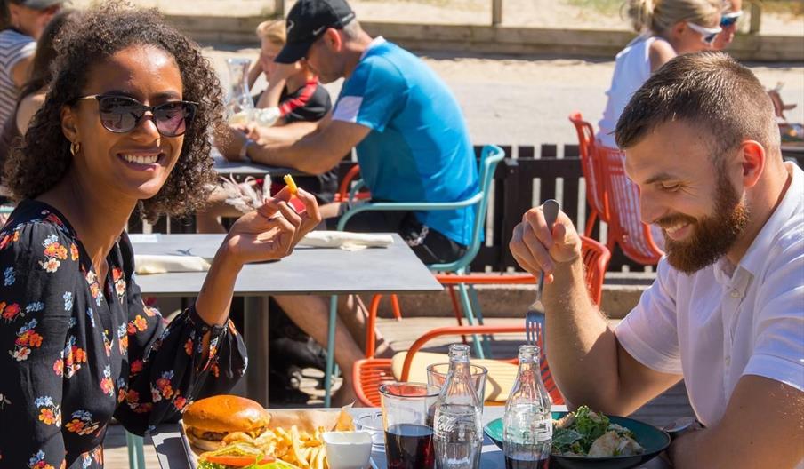 Bilde av gjester som spiser, en med burger og pommes frites, og en med kyllingsalat.