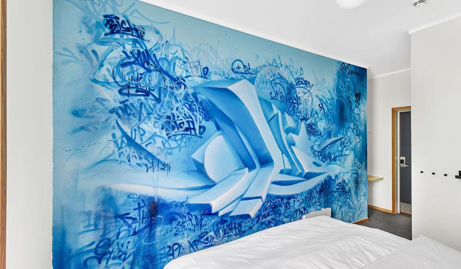 hotellvegg med streetart i blått med signaturer og noe som ser ut som 3D og virker som om det står ut fra veggen.