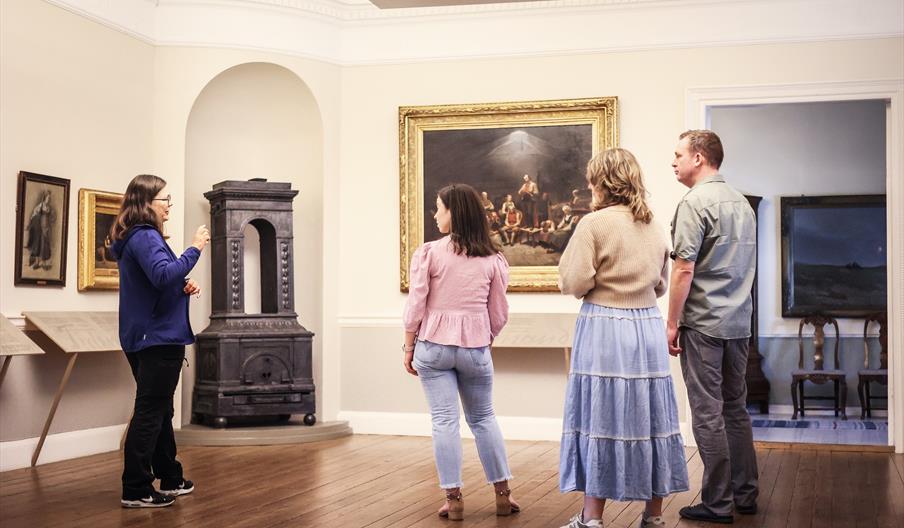 Fire personer inne på museet ser på det store maleriet «Haugianerne» på Mandal museum, der Adolph Tidemand skildrer lekpredikanten Hans Nielsen Hauges følgere.