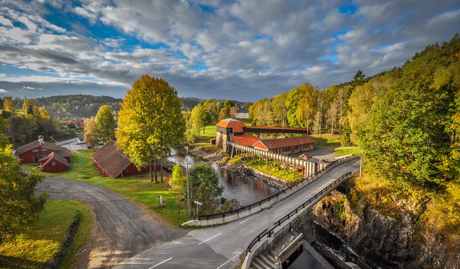 bilde av Næs jernverksmuseum og omgivelsene rundt som består av skog, veier og en elv.