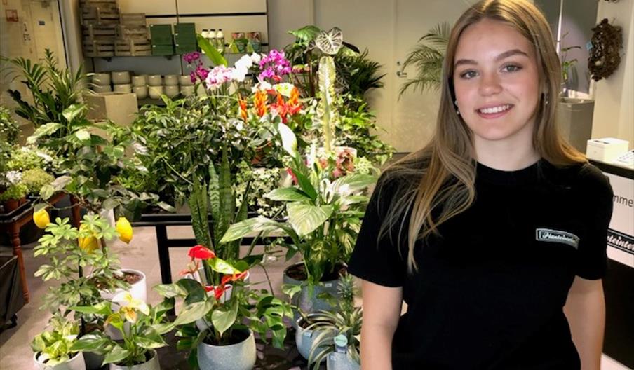 Smilende jente i svart t-skjorte foran blomster og planter.