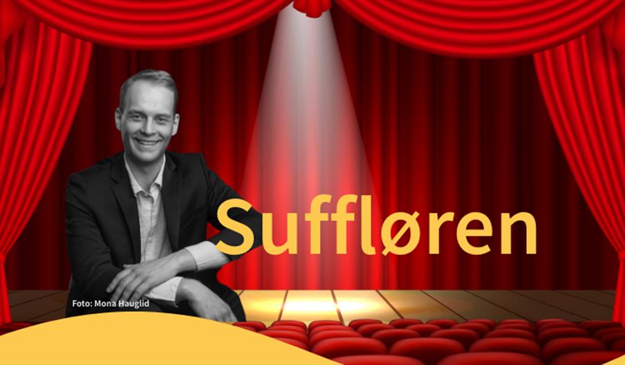 mann i dress sittende foran en teaterscene med røde forheng