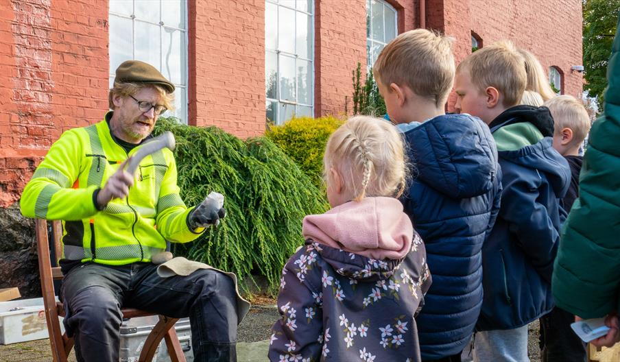 Flintsmed som viser interesserte barn hva han jobber med