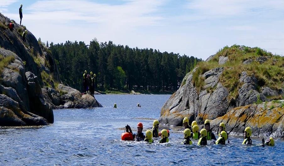 gruppe med mennesker i vannet med hjelm og våtdrakt klare for litt coasteering