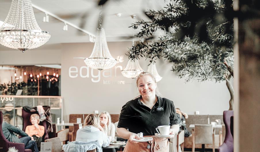 Smilende kvinne i Edgars uniform med kaffe i hendene