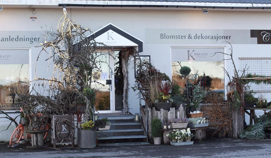 Bilde på utsiden av butikken med masse blomsterdekorasjoner rundt inngangspartiet.