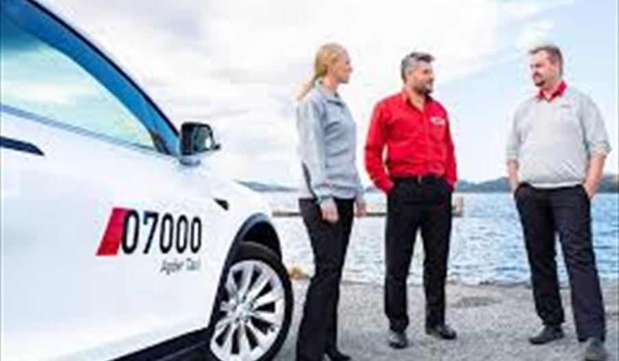 Taxi og tre personer som står foran sjøsanden