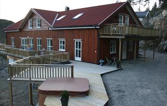 Brun hytte med balkong og terasse. Jacuzzi boblebad på terrassen.
