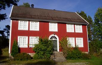 Annen rød bygning med hvite karmer, 9 vinduer og 1 grønn dør