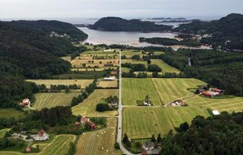 Bilde tatt ovenfor av en vei midt på med åkere og hus på høyre og venstre side