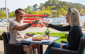 To personer med hvert sitt glass og skåler. Sitter ute i finværet, med en pizza på bordet