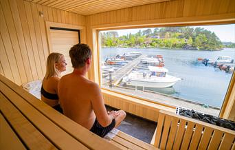 sauna-badstue-tregde-mandal-bading-skjærgård-utsikt. To personer i badstue hos Tregde Sauna. Foto.