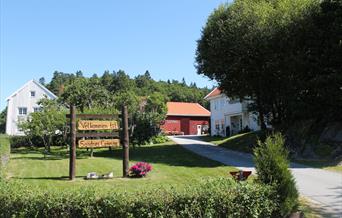 Innkjørsel til Sandnescampingen. Stort treskilt som står "Velkmmen til Sandes Camping" i en hage.
