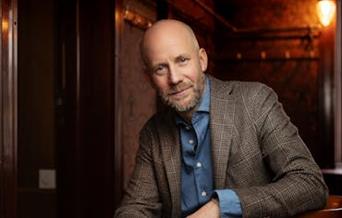 Portrett av forfatter Johan B. Mjønes i brun jakke og blå skjorte.