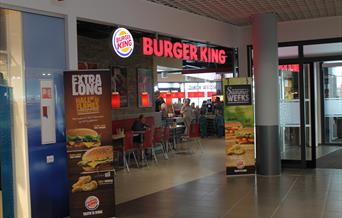 inngangen til Burger king, Alti Mandal. Store bokstaver ved taket "burger king" + logo. høye bannere på hver sin side av inngangen med bilde av burgere.