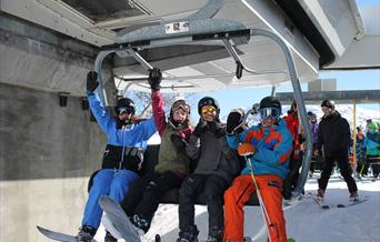 Fire glade ungdommer med ski sitter i stolheisen, bilde