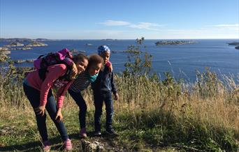 Tre barn på toppen av utsiktpunktet med havet bak seg og åpen himmel