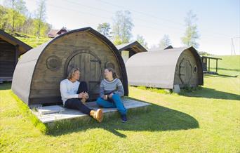 Jente og gutt sitter å ler sammen foran en av hobbithyttene til Adventure Norway