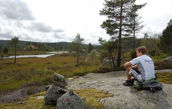 Bilde av en mann som sitter på sekken sin og ser ut mot landskapet med vanndam