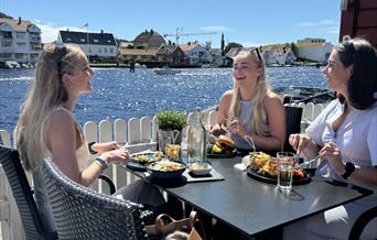 Tre jenter som smiler og spiser god mat hos Brygga