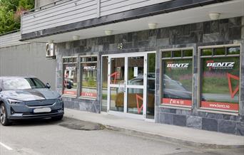 Fasaden til Bentz Trafikkskole i Alleen i Lyngdal sentrum, med store vinduer og logo.