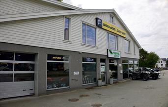 Fasaden til Trippel Motor Lyngdal i Alleen, med logo og utstilte ATV-er foran butikken.