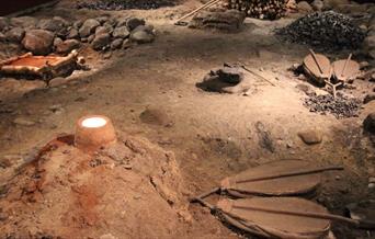 Bilder av rekonstruert jervinnetuft med smelteovn og blåsebelger, røstet jernmalm og kolgrop med trekull.