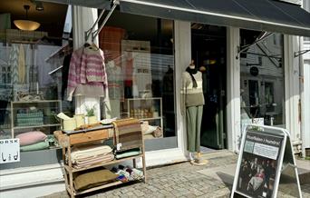 Fasade til butikken Husfliden i gågata, med åpen dør og flotte utstillinger av strikkede gensere