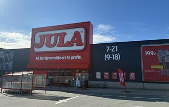 Inngangen til Jula Lyngdal i Handelsparken, med rød logo, handlevogner og åpningstider på fasaden.